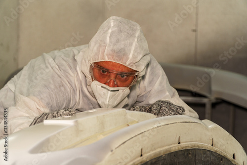 Worker in protective gear applying finishing touches to a white mold in a manufacturing facility during daytime