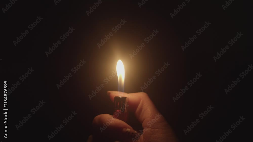 Woman's hand with a gas lighter. A woman kindles a fire. light fire gas lighter in the dark. a lighter flame on a black background. ignited by sparks. The lighter.