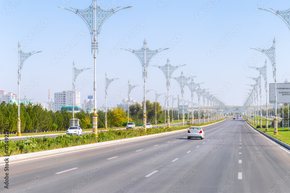 Fototapeta premium Straight avenue leading towards central landmarks of Ashgabat, lined with streetlights and surrounded by greenery. Turkmenistan