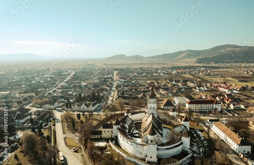 Vast landscapes unfold as Piatra Craiului mountains rise majestically above Rasnov and Plaiul Foii, blending nature's beauty with charming Romanian architecture under a clear sky photo