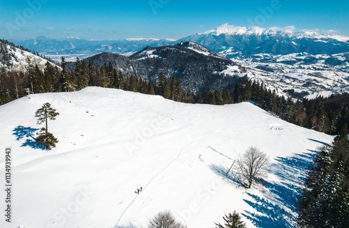 Majestic snow blankets the Piatra Craiului mountains near Rasnov, creating a serene winter wonderland. Enthusiasts explore the pristine landscape under a clear blue sky photo