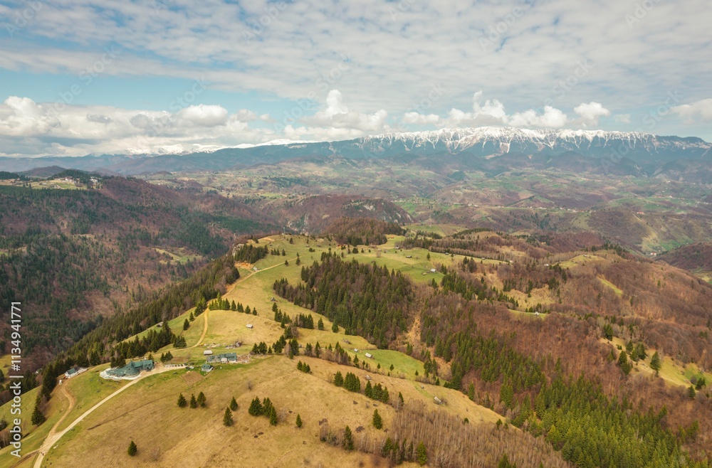 Vast green valleys and rugged mountains create a stunning backdrop in this aerial view of Piatra Craiului, showcasing the natural beauty of Brasov's landscape under a bright sky Vast green valleys and rugged mountains create a stunning backdrop in this aerial view of Piatra Craiului, showcasing the natural beauty of Brasov's landscape under a bright sky