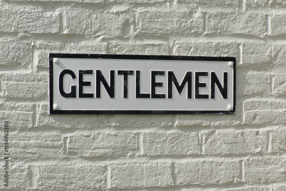Sign for Gentlemen's toilet. Black lettering on white background on white brick wall. Sign for Gentlemen's toilet. Black lettering on white background on white brick wall.
