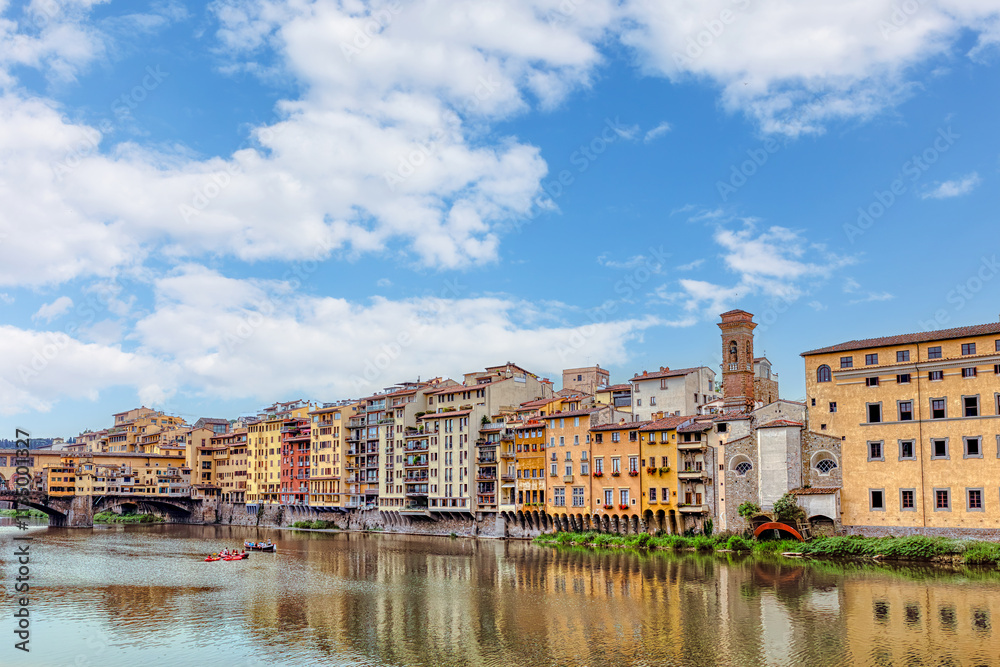 Colorful medieval houses sit above the Arno River in Florence, showcasing vibrant facades and historical architecture under blue cloudy sky. Colorful medieval houses sit above the Arno River in Florence, showcasing vibrant facades and historical architecture under blue cloudy sky.