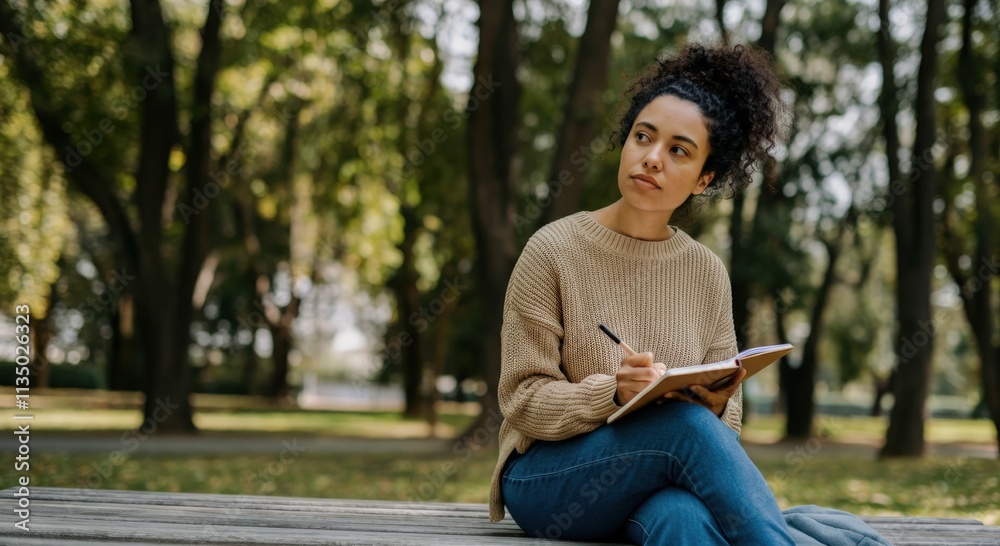 Thoughtful young hispanic woman writing in notebook at park bench on an autumn day for journaling inspiration