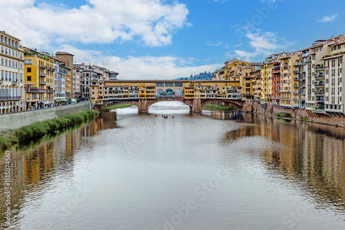 Fototapeta Naklejka Na Ścianę i Meble -  Medieval Florence showcases its stunning architecture with colorful buildings lining the Arno River, where boats glide smoothly along the reflective waters under a bright sky.