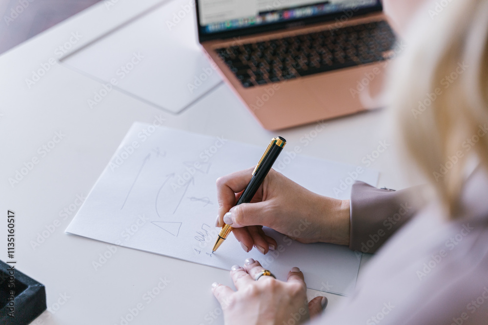 European business woman CEO working on laptop sitting at table workspace, making notes in office.