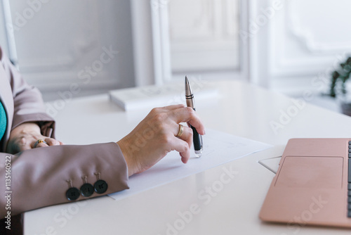 Obraz na płótnie A closeup of a hand holding a sleek pen, writing on a blank sheet in a stylish and professional office w salonie