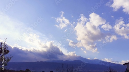 Veduta panoramica dell'Etna con cielo azzurro e qualche nuvoletta bianca illuminata dal sole.