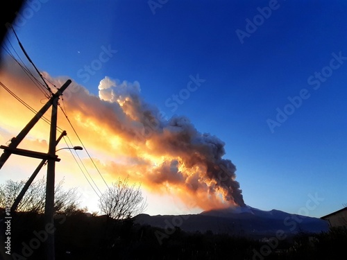Un imponente sbuffo di sabbia vulcanica dell'Etna durante un'eruzione, infiammato dalle luci del tramonto.