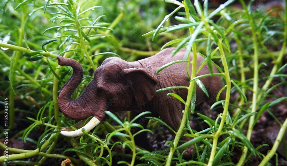 elephant in the bush, close up photo of cute elephant toy is in the grass and green plants, looks real elephant in the bush, close up photo of cute elephant toy is in the grass and green plants, looks real