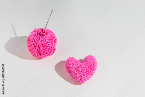 Crochet pink heart with ball of yarn and hook on light background, top view photo