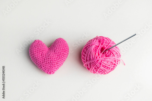 Crochet pink heart, ball of yarn and a crochet hook on light background, top view photo