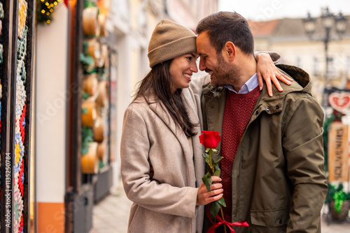 Mid adult Caucasian couple indulges in romantic window shopping during Valentine's Day. The woman holds a rose and wears a cozy coat, while the man sports a warm jacket. photo