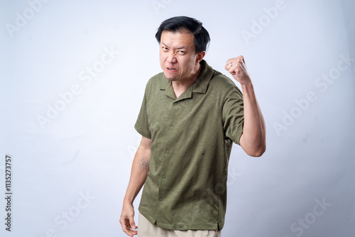 Фотография An Asian man in a green shirt shows anger and determination with a clenched fist