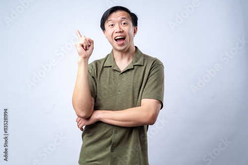 Photography An Asian man in a casual green shirt excitedly points upward with one finger, mouth open in expression, standing against a clean white background