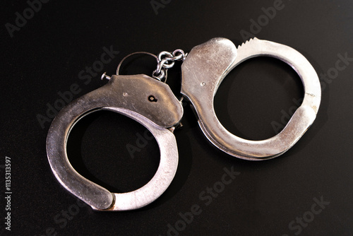 Fototapet Pair of handcuffs used by law enforcement to arrest criminals on a black background