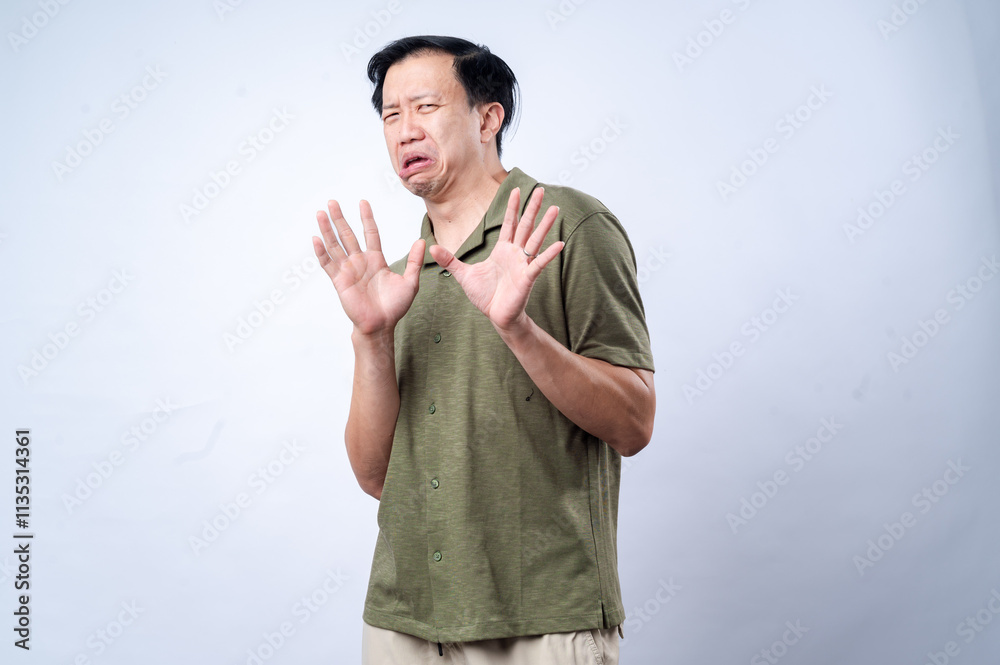 Naklejka premium An Asian man in a green shirt with a worried or disgusted facial expression, holding both hands up as if signaling 