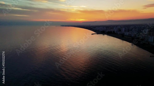 Wallpaper Mural Stunning sunset casts orange and yellow hues across the sky, illuminating the mediterranean sea. Buildings gracefully line the coast, creating a picturesque urban landscape at dusk Torontodigital.ca