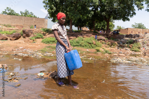 Young African woman standind with her canister in the middle of a flooded road wondering where she will get clean drinking water after her whole village was inundated