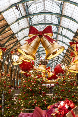 London, UK - December 2, 2024, Christmas-decorated Covent Garden. A view through fir trees of red bells and ornaments.