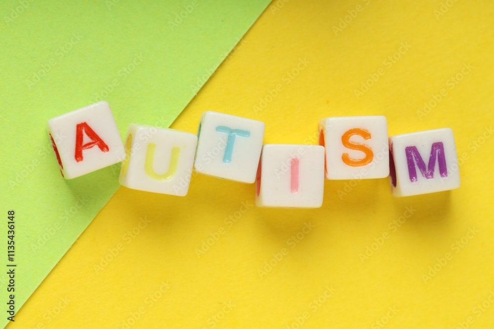 Obraz premium Word Autism made with colorful cubes and green sheet of paper on yellow background, top view