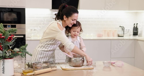 pretty mother and her cute little child daughter in aprons preparing the dough in the kitchen, bake Christmas cookies