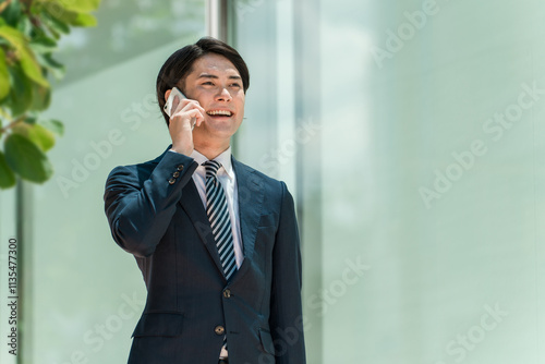 スマホで商談しながら出勤・出社・通勤する若い男性アジア人ビジネスマン

