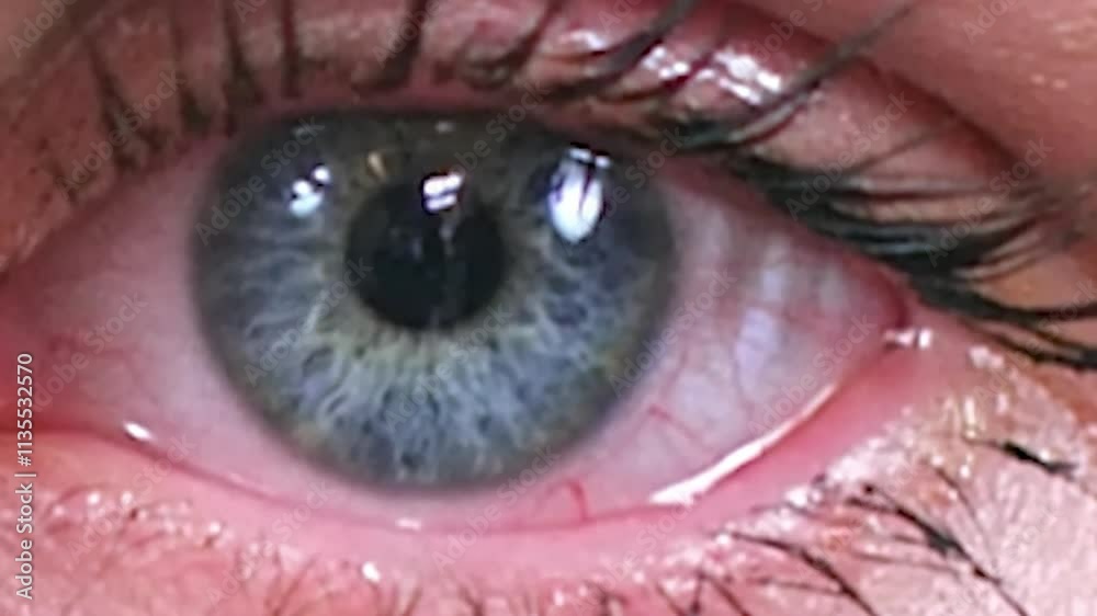 Close-up of a gray-blue woman eye with tear rolling down, showcasing intricate details of the iris, pupil, and surrounding blood vessels.