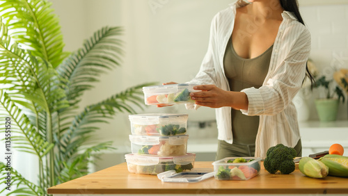 Attractive woman arranging her meal prep containers on the kitchen counter, ready for a week of healthy eating. Healthy lifestyle and nutrition concept.