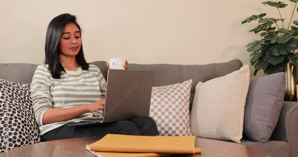 South Asian tired young woman sitting on the couch yawning while working on the laptop South Asian tired young woman sitting on the couch yawning while working on the laptop