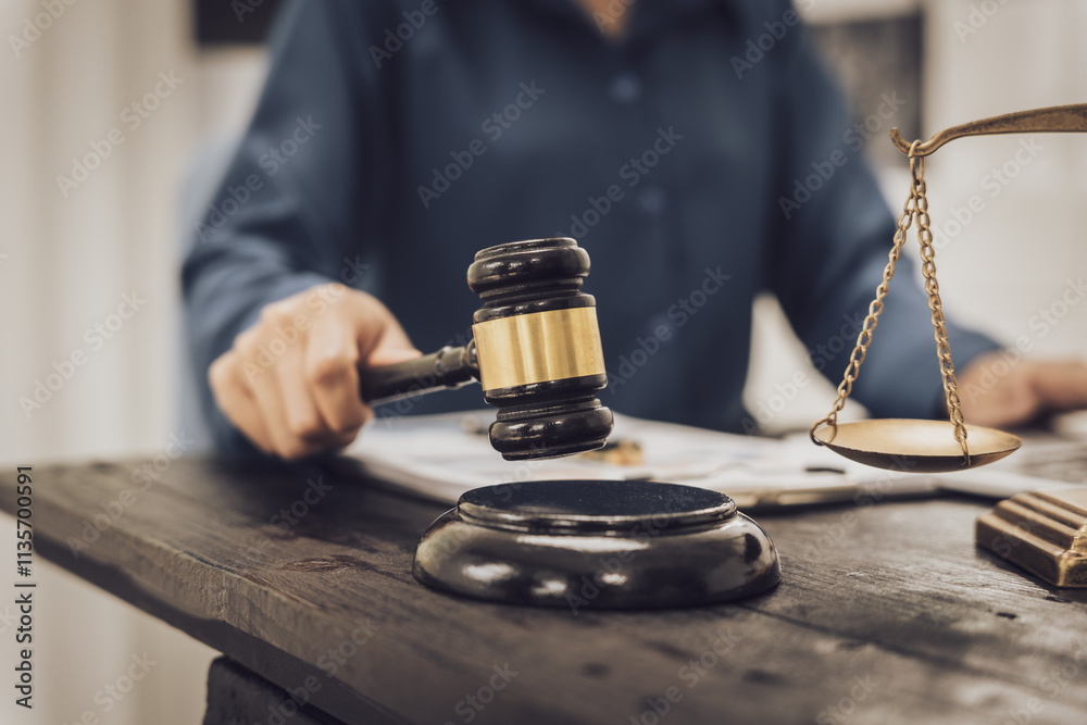 Close-up of an Asian female lawyer sitting at her desk in a law office. A wooden hammer and brass scales symbolize justice. She demonstrates expertise in the legal and justice process Close-up of an Asian female lawyer sitting at her desk in a law office. A wooden hammer and brass scales symbolize justice. She demonstrates expertise in the legal and justice process