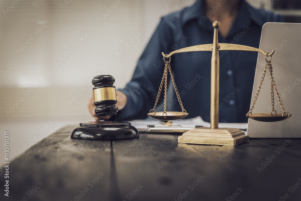Close-up of an Asian female lawyer sitting at her desk in a law office. A wooden hammer and brass scales symbolize justice. She demonstrates expertise in the legal and justice process Close-up of an Asian female lawyer sitting at her desk in a law office. A wooden hammer and brass scales symbolize justice. She demonstrates expertise in the legal and justice process