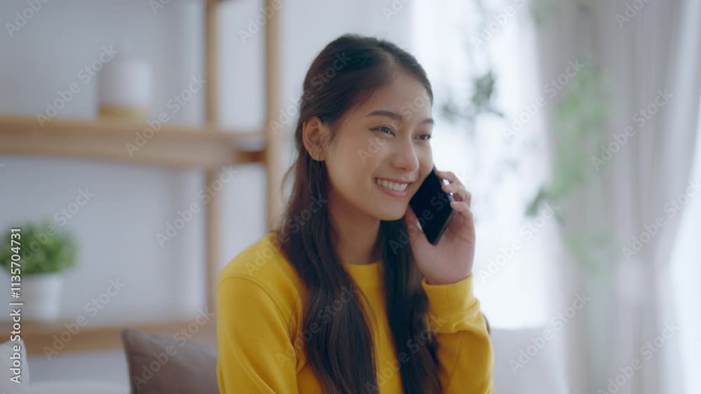 Happy young asian woman speaking on mobile phone at home, Female teen answering call on cellphone while sitting in couch. Asia girl talking on smartphone Happy young asian woman speaking on mobile phone at home, Female teen answering call on cellphone while sitting in couch. Asia girl talking on smartphone