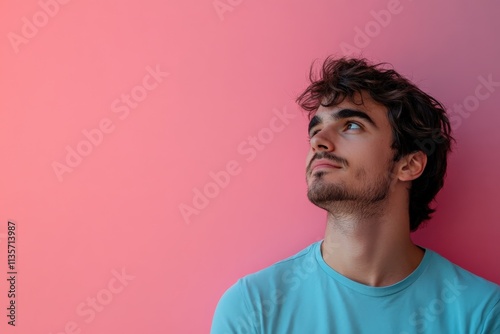 Thoughtful Young Man Gazing Upward Against a Soft Pink Background