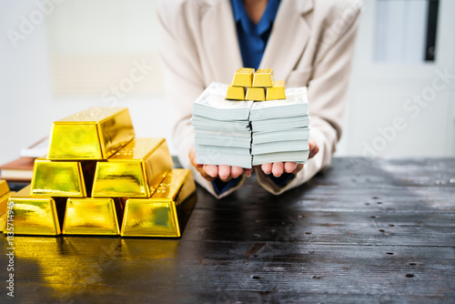 An Asian businesswoman sits at her desk analyzing gold bar prices, buying and selling gold, trading gold stocks, monitoring charts, and studying currency trends in an uptrending stock market. photo