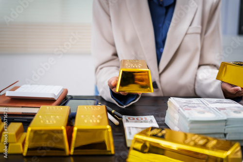 An Asian businesswoman sits at her desk analyzing gold bar prices, buying and selling gold, trading gold stocks, monitoring charts, and studying currency trends in an uptrending stock market. photo