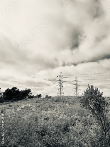 Black and white image of power lines stretching across a dramatic sky filled with dramatic clouds.