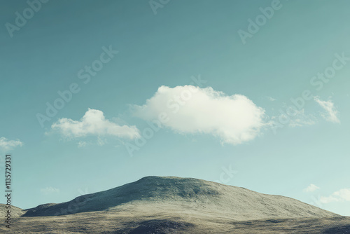 Soft clouds drift over a gentle hill under a clear blue sky in a serene landscape photo