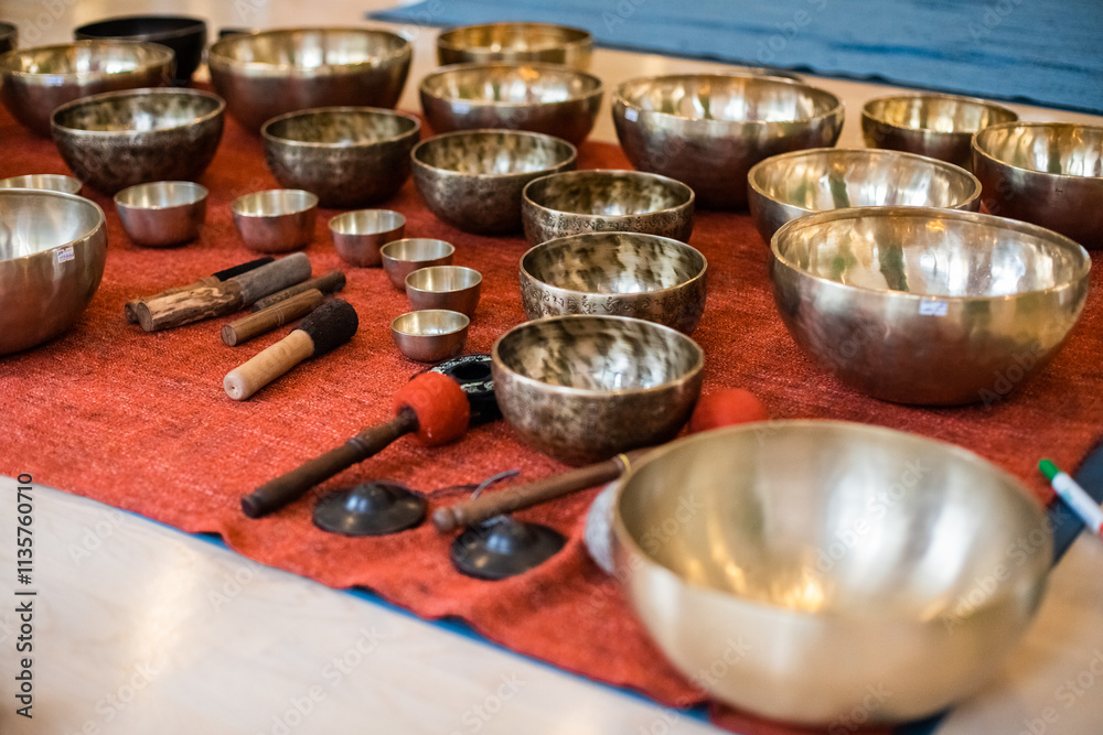 An arrangement of Tibetan singing bowls of various sizes on a red mat with mallets and tools, creating a tranquil setup for sound healing or meditation sessions