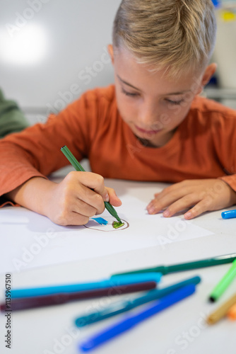 Young boy drawing with markers at school desk: concentrated child enjoying art class