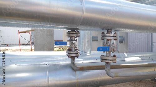 Metal pipes showcase valves with blue handles, regulating the flow of various fluids. Positioned on large, insulated pipes, these valves operate within an industrial environment.Heavy industry concept