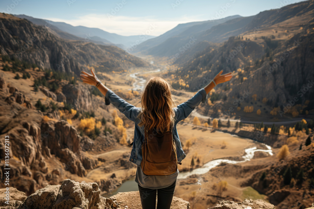 Naklejka premium Rear view of a girl sitting with her arms raised and contemplating the beauty of the mountains and river.