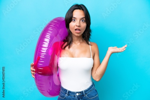 Young hispanic woman holding air mattress donut isolated on blue background with shocked facial expression photo