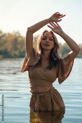 Portret kobiety w kremowym kombinezonie w wodzie z rękami uniesionymi