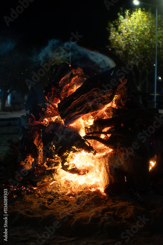 A traditional Madeiro bonfire in Livramento, Mafra, Portugal, glowing under night skies. The massive logs ablaze create an orange glow, symbolizing a festive cultural gathering with rustic warmth.