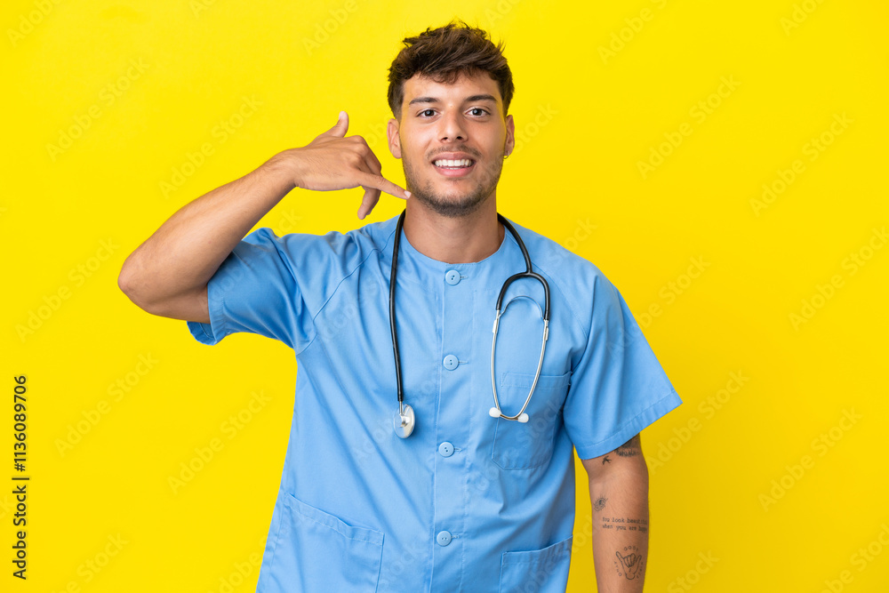 Young surgeon doctor man isolated on yellow background making phone gesture. Call me back sign Young surgeon doctor man isolated on yellow background making phone gesture. Call me back sign