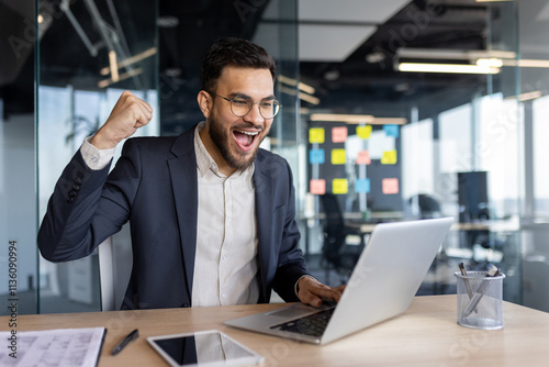 Mature businessman rejoices success working on a laptop in a professional setting. The image conveys concepts like achievement, corporate enthusiasm, and technological adeptness.