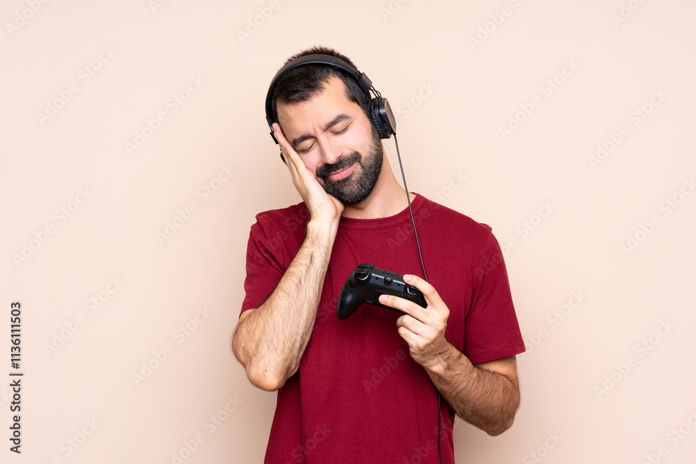 Fotografie Man playing with a video game controller over isolated wall making sleep gesture