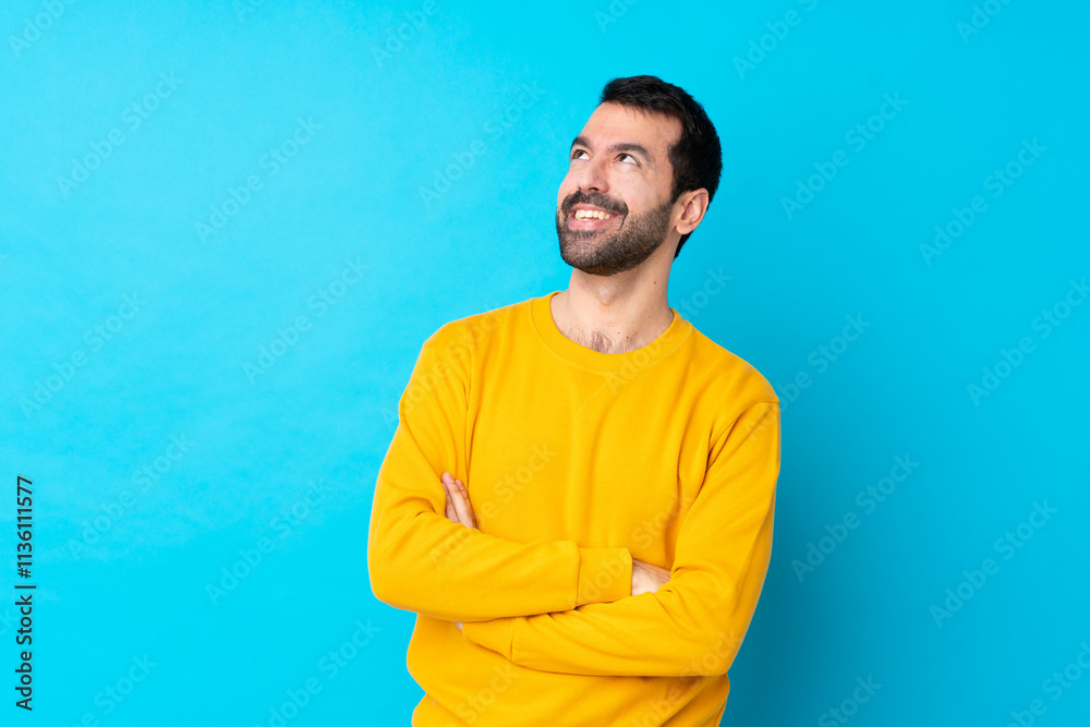 Young caucasian man over isolated blue background looking up while smiling